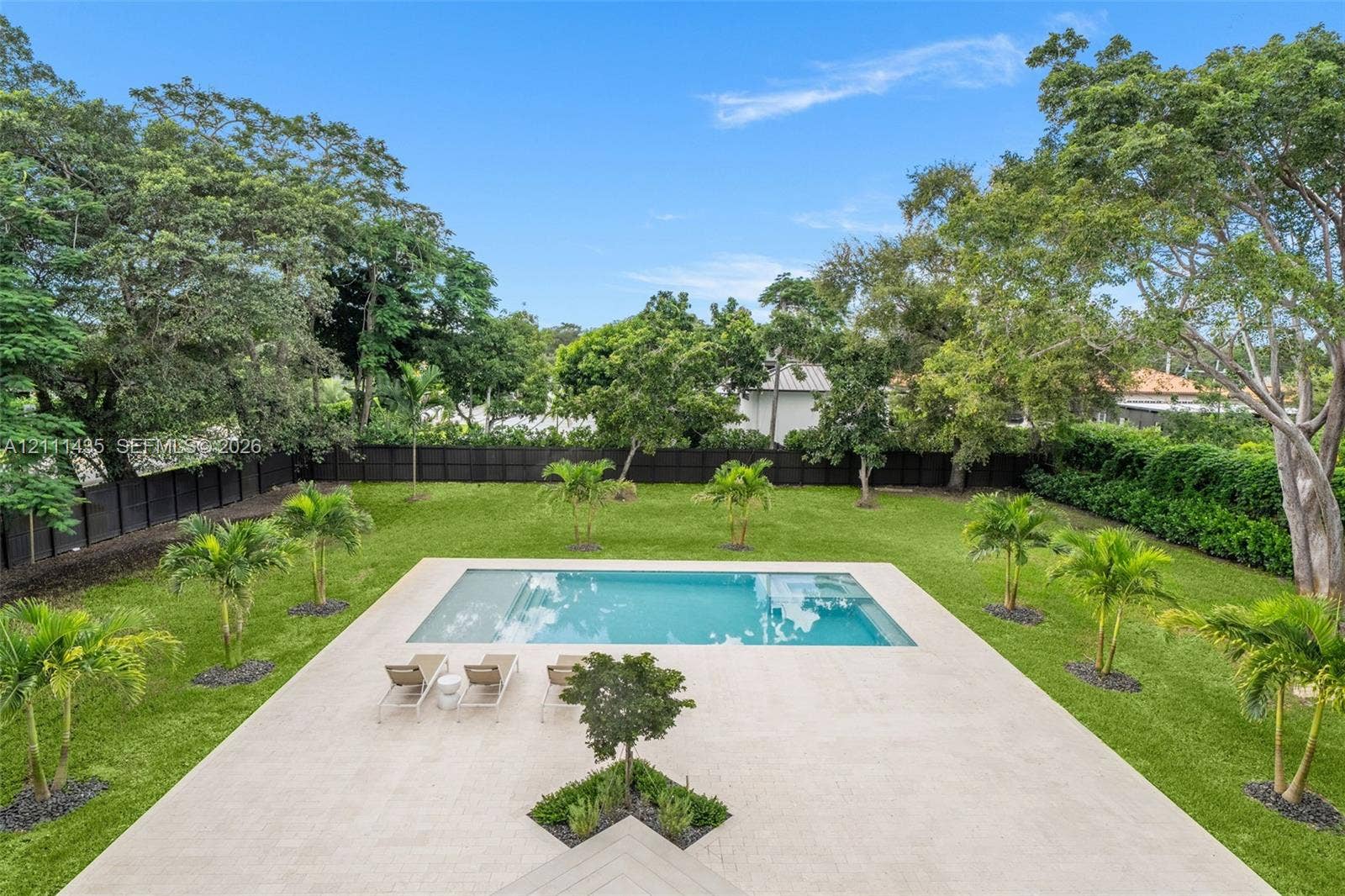 9530 SW 95th Court, Miami, FL 33176 Expansive backyard featuring an in-ground swimming pool, light-toned concrete patio, manicured lawn, perimeter fencing, and mature trees