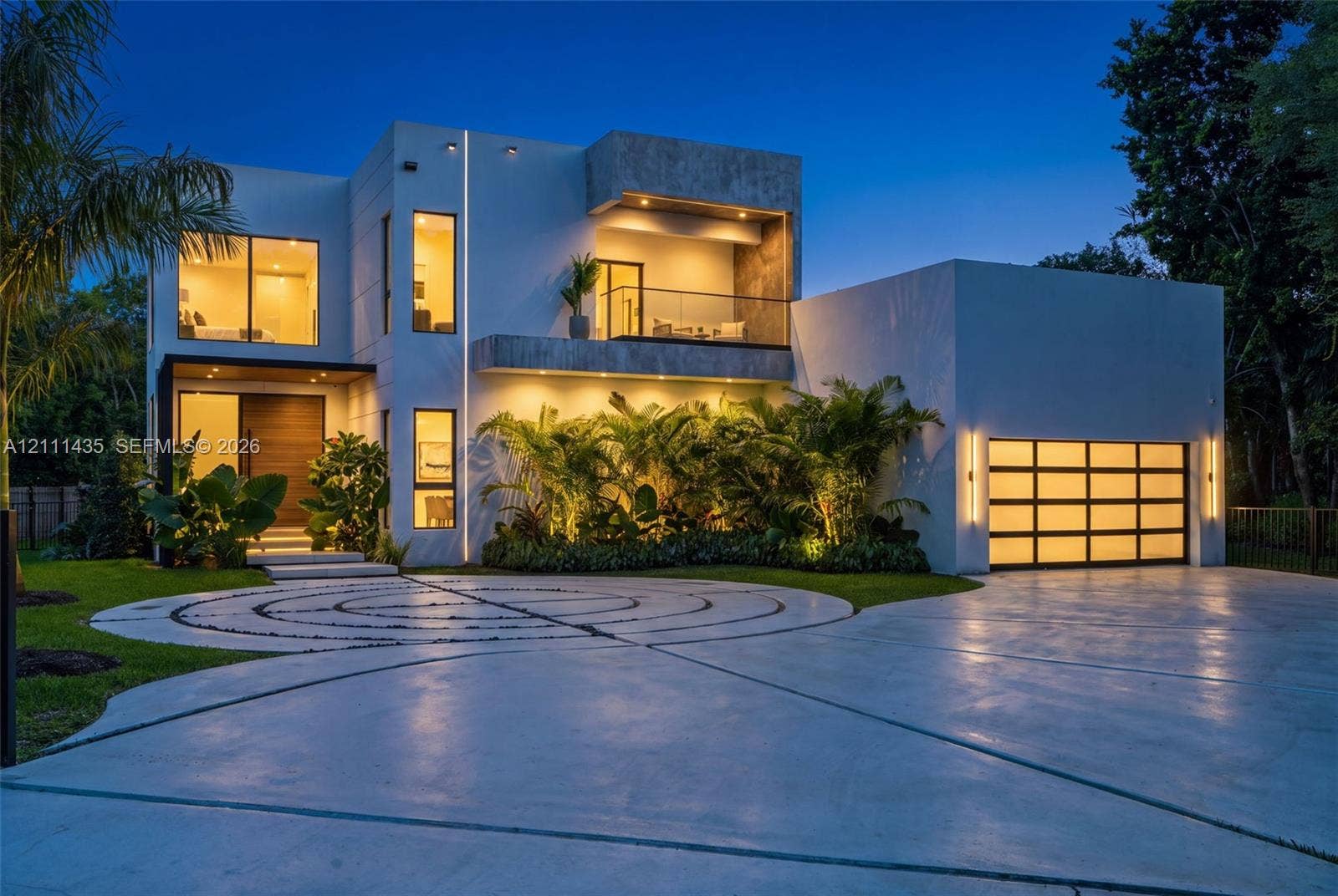 9530 SW 95th Court, Miami, FL 33176 Modern architectural exterior featuring smooth stucco siding, an upper-level glass-railed balcony, a multi-pane glass garage door, and a geometric concrete driveway