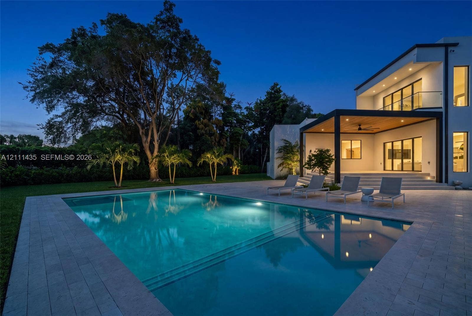 9530 SW 95th Court, Miami, FL 33176 Modern architectural exterior featuring a swimming pool with integrated stairs, expansive stone paver pool deck, covered patio with wood-paneled ceiling, and second-story balcony with glass railing