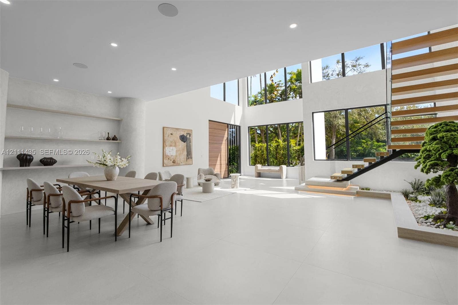 9530 SW 95th Court, Miami, FL 33176 Double-height living area featuring large-format tile flooring, floor-to-ceiling windows, custom built-in recessed shelving, and a floating staircase with integrated lighting
