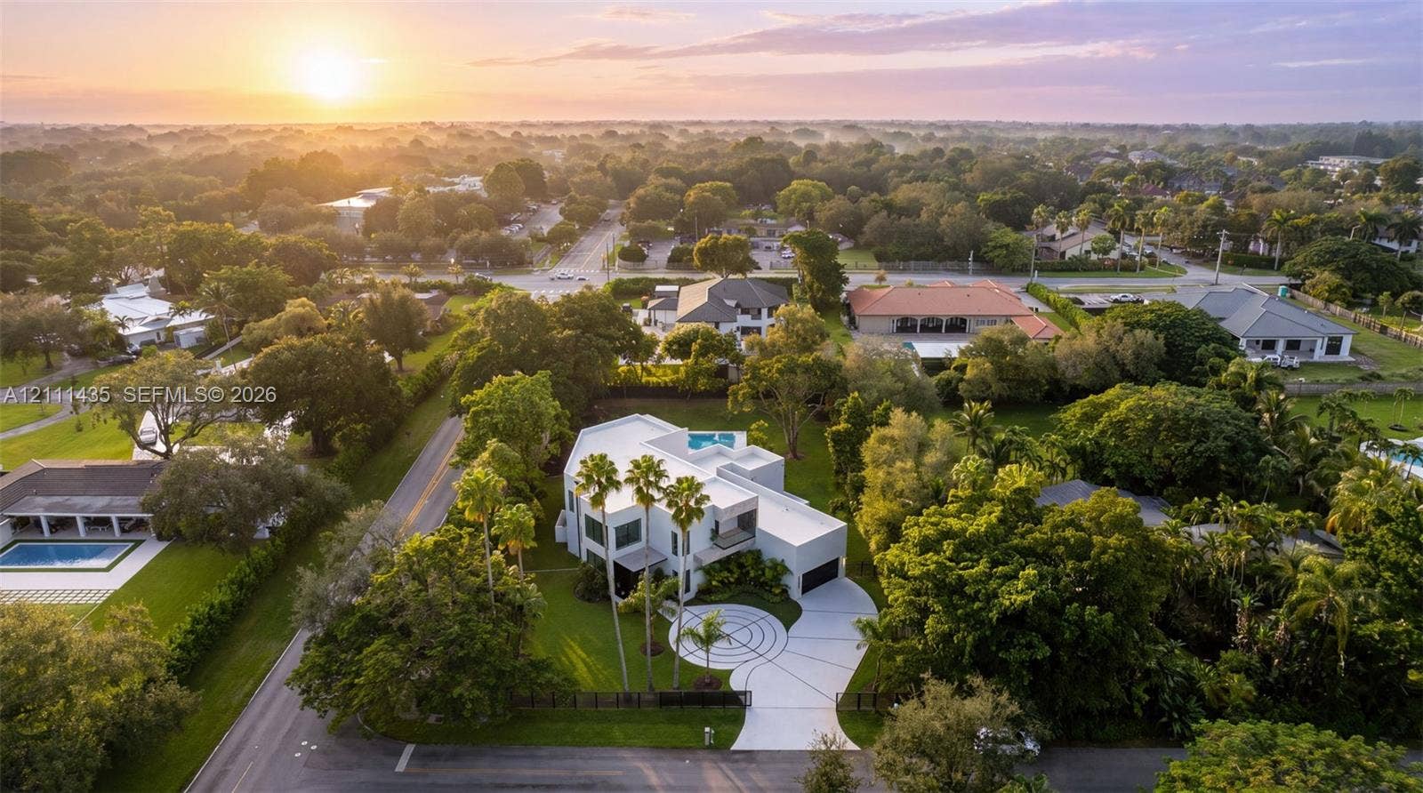 9530 SW 95th Court, Miami, FL 33176 Aerial perspective of a multi-level contemporary residence featuring a flat roofline, circular concrete driveway, private rooftop pool, and mature perimeter landscaping