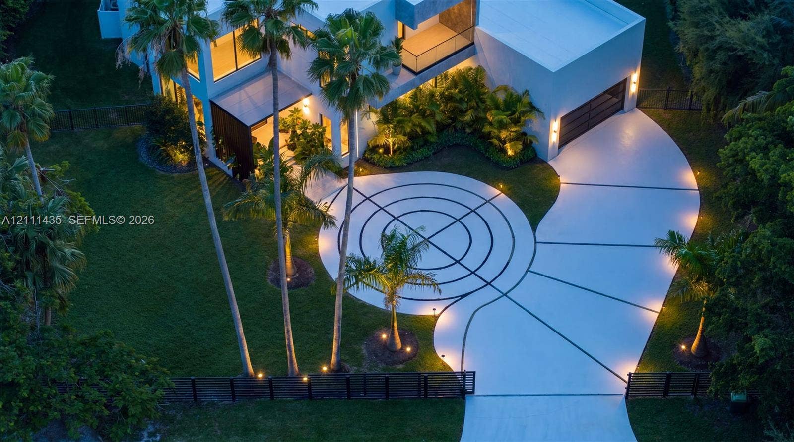 9530 SW 95th Court, Miami, FL 33176 Contemporary architectural exterior featuring a geometric patterned driveway, expansive manicured lawn, multi-level structure with integrated lighting, and mature palm landscaping
