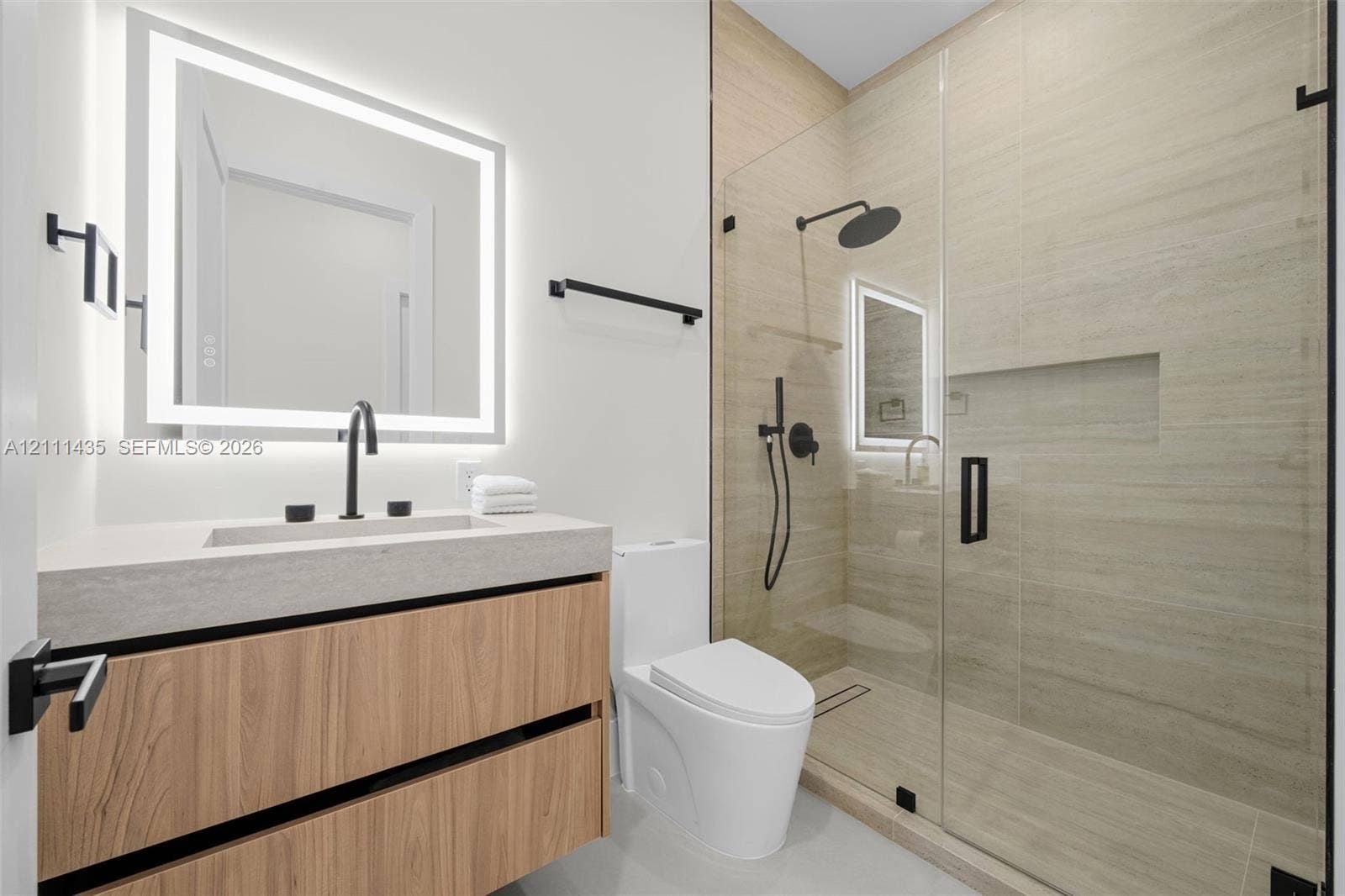 9530 SW 95th Court, Miami, FL 33176 Floating wood-finish vanity with a rectangular sink, integrated LED-backlit mirror, walk-in shower with a glass enclosure and built-in recessed shelving, and matte black fixtures