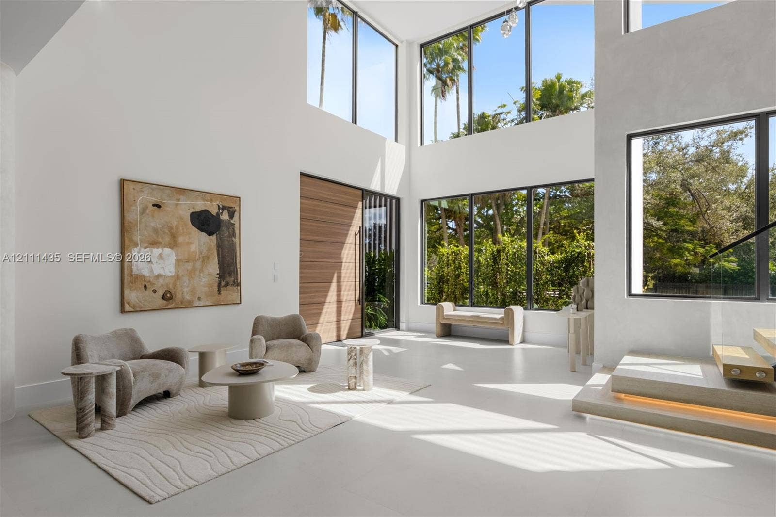 9530 SW 95th Court, Miami, FL 33176 Double-height living area featuring floor-to-ceiling windows, polished concrete flooring, a natural wood entry door, and a floating staircase with integrated lighting