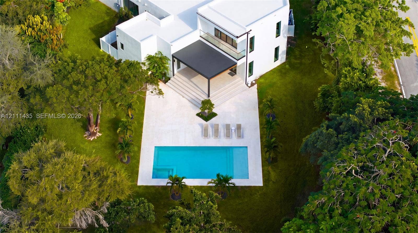 9530 SW 95th Court, Miami, FL 33176 Contemporary residence featuring a white stucco exterior, covered patio, rectangular swimming pool, stone-paver pool deck, and mature landscaping
