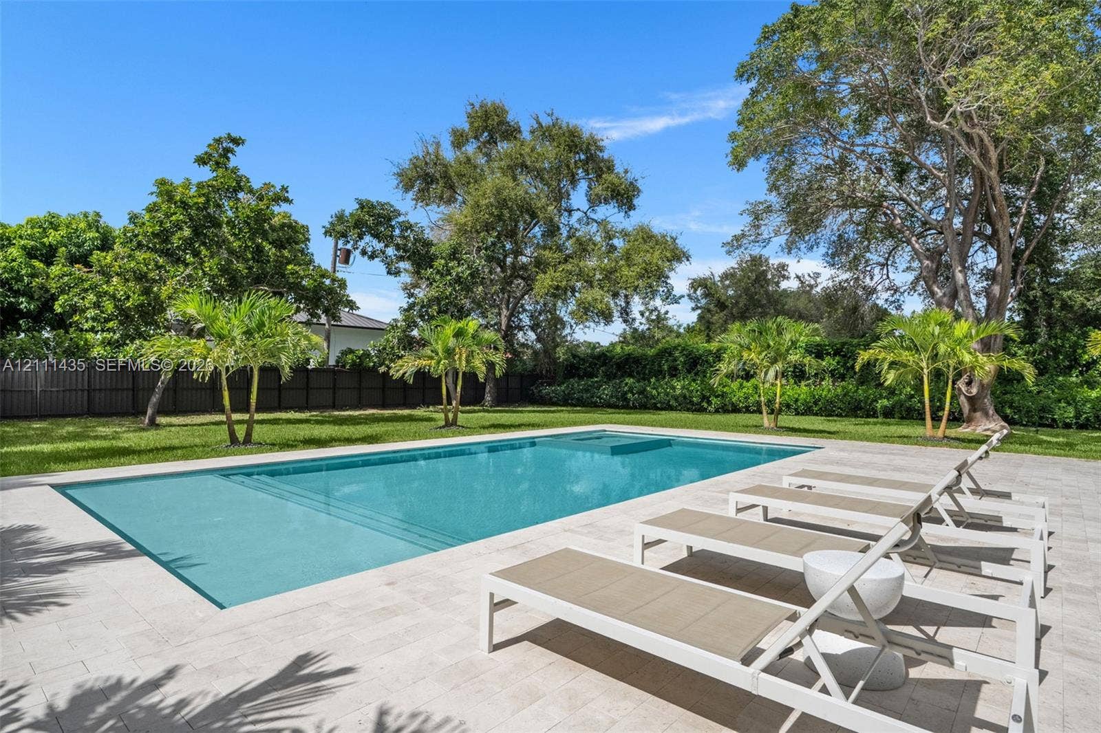 9530 SW 95th Court, Miami, FL 33176 Rectangular swimming pool with integrated sun shelf and spa, surrounded by stone-finish paver decking, expansive grass lawn, mature trees, and privacy fencing