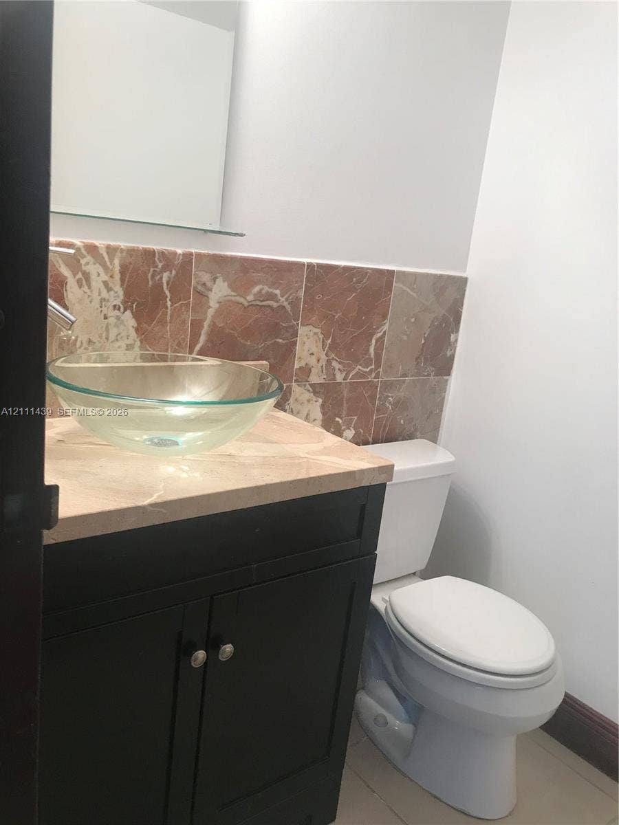 800 Parkview Drive, #102, Hallandale Beach, Hallandale Beach, FL 33009 Half bathroom Dark finish vanity featuring a stone countertop, glass vessel sink, wall-mounted mirror, and decorative stone tile backsplash