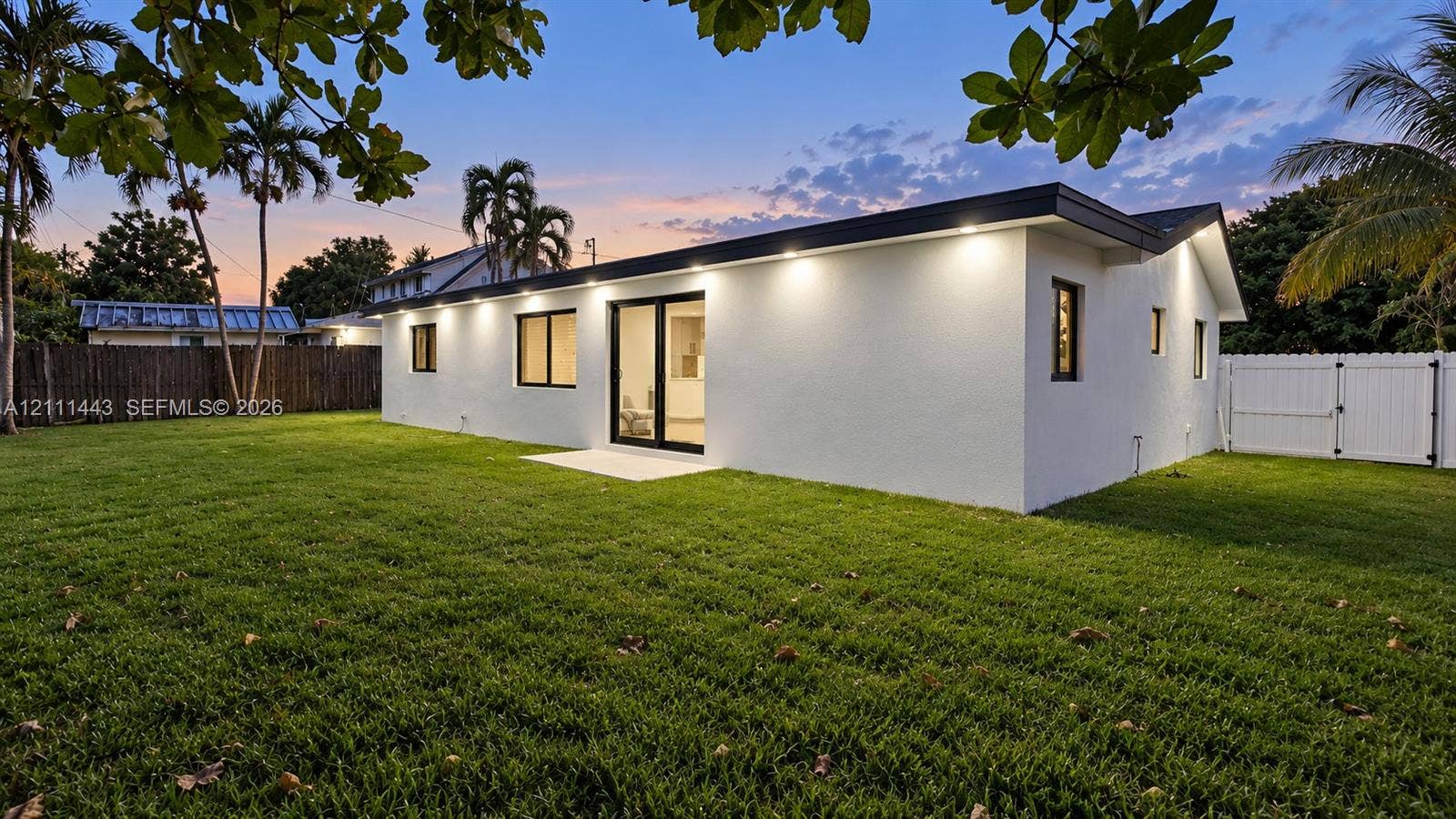Expansive backyard featuring a level lawn, white perimeter fencing, and recessed exterior soffit lighting