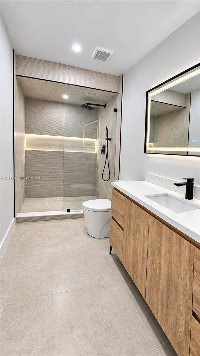 Walk-in shower with integrated wall lighting and matte black rainfall fixture, wood-finish floating vanity with quartz countertop, and rectangular LED-backlit mirror
