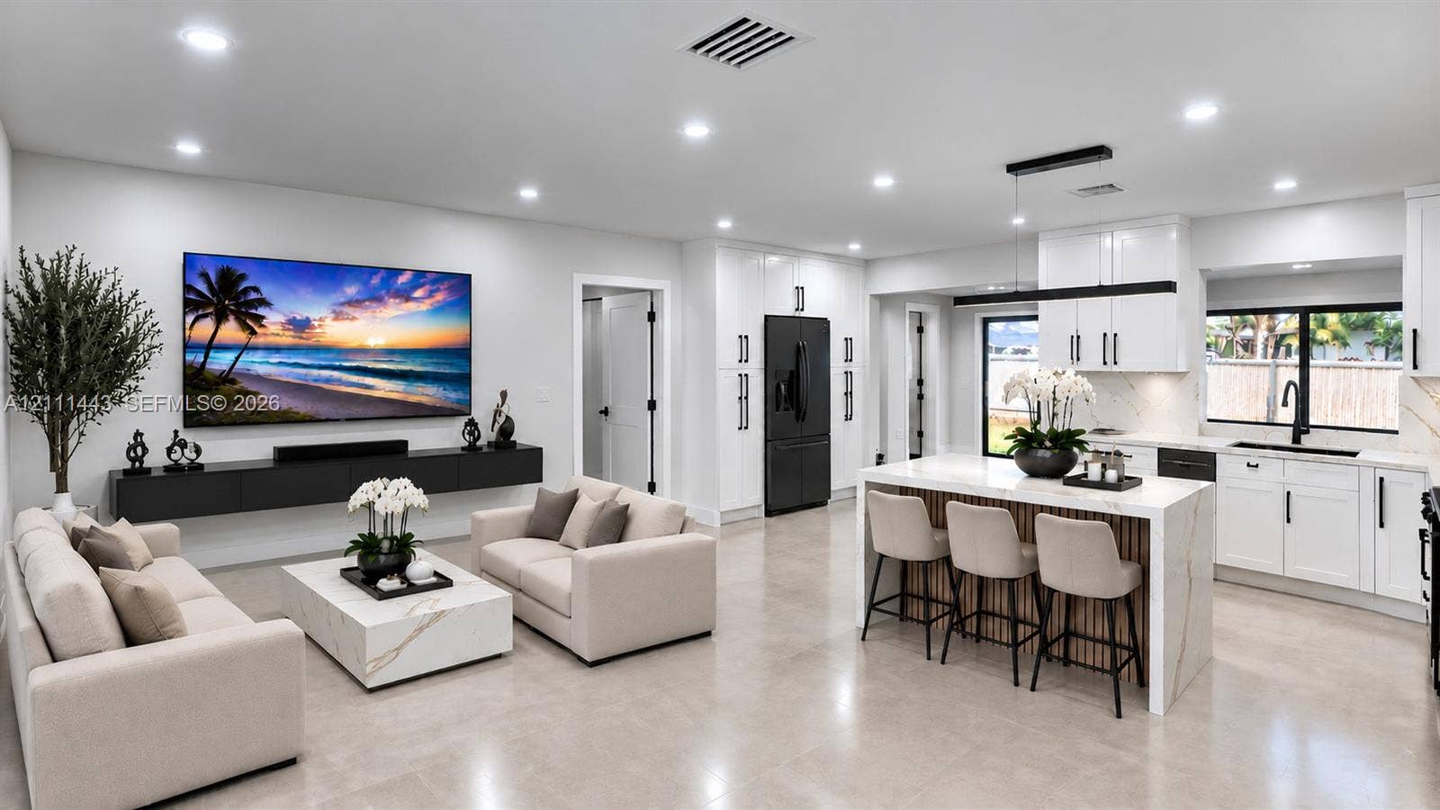 Open-concept living space featuring high-gloss white cabinetry, a large kitchen island with stone-finish countertops, floating wall-mounted storage, recessed lighting, and large-format tile flooring