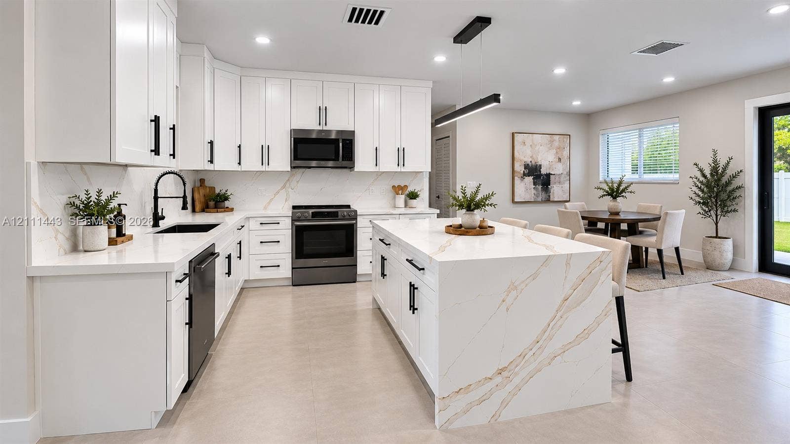 Digitally Staged - Kitchen featuring white shaker-style cabinetry, an expansive center island with waterfall edge stone countertops, high-contrast matte black hardware, integrated stainless steel appliances, and matching stone backsplash
