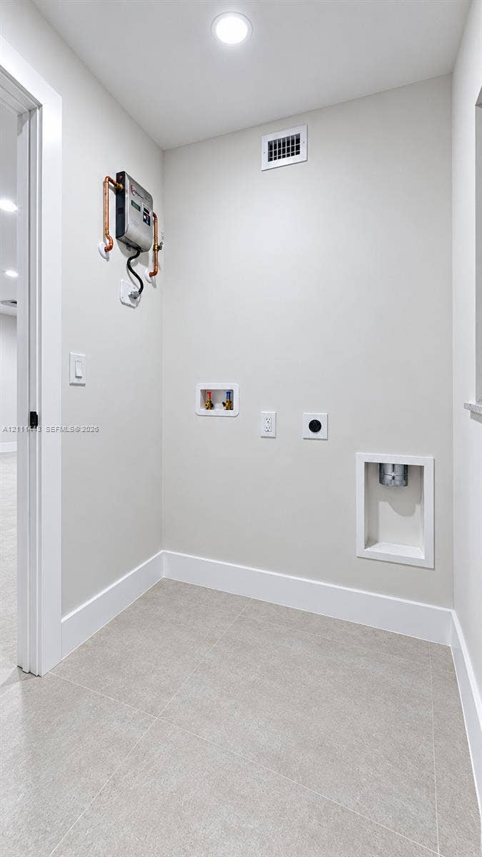 Utility area featuring neutral tile flooring, recessed dryer vent, wall-mounted water shut-off valves, and recessed plumbing hookups