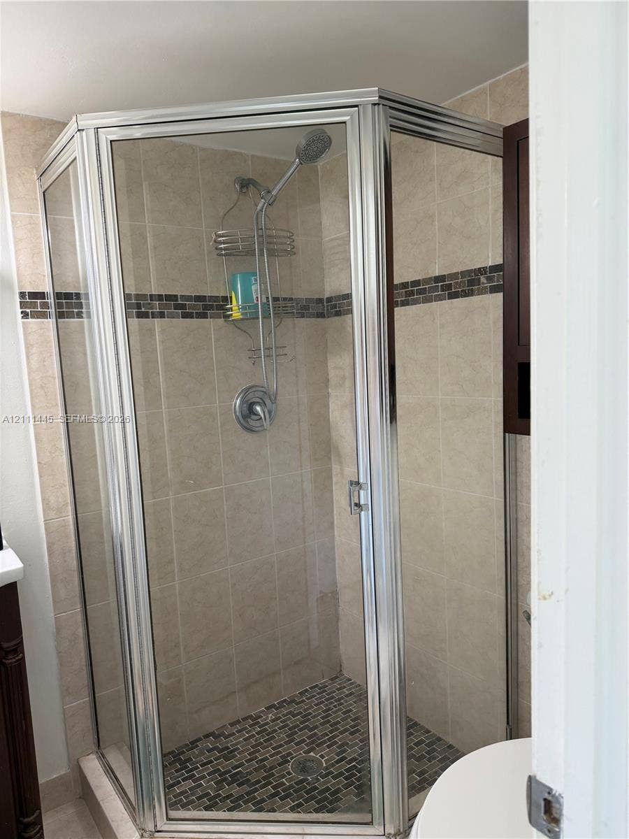 8255 Abbott Avenue, #402, Miami Beach, Miami Beach, FL 33141 Corner shower enclosure featuring a metal frame, tile wall surround, stone-tiled floor, decorative glass tile accent strip, and a chrome hand-held shower fixture
