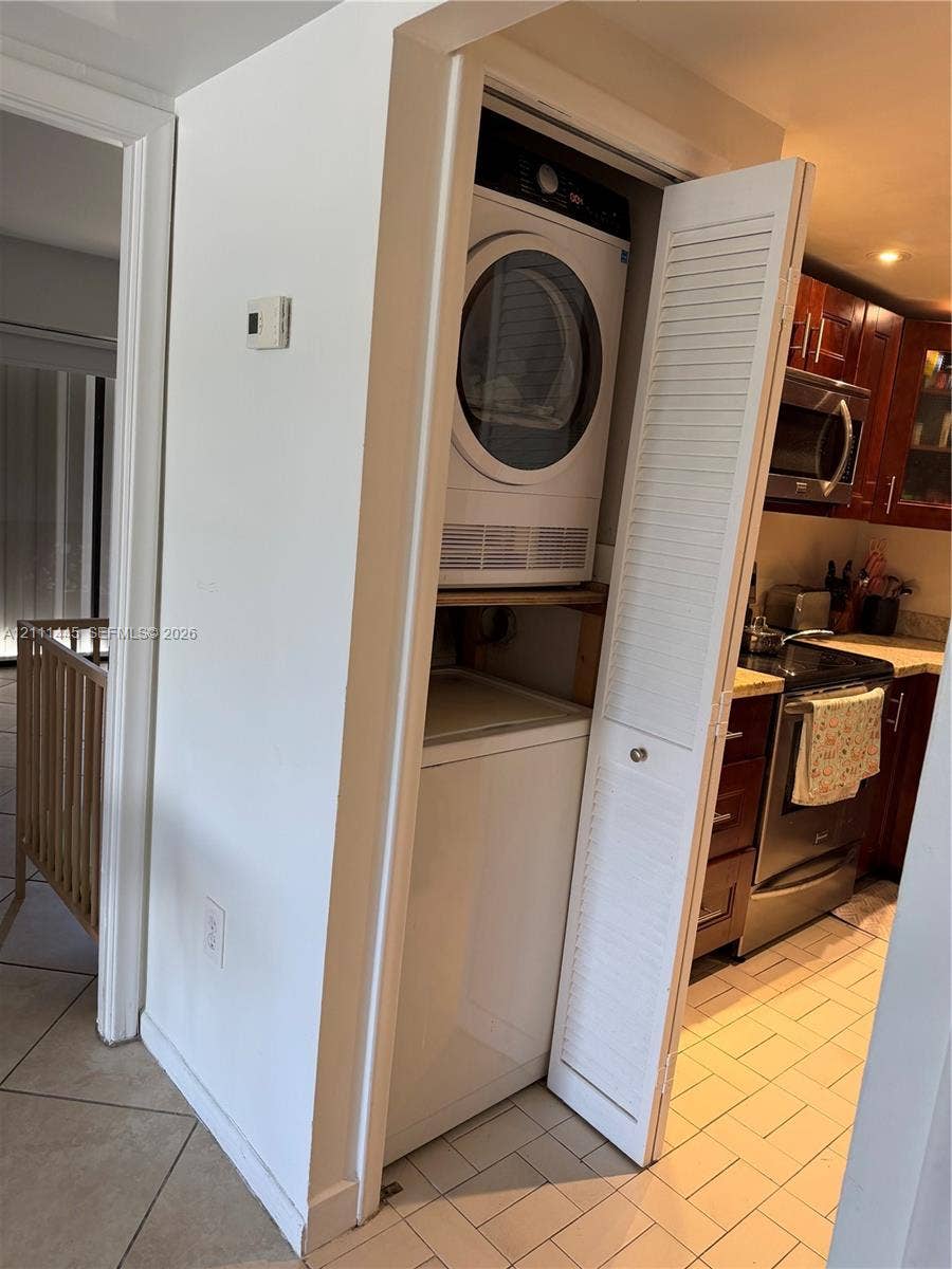 8255 Abbott Avenue, #402, Miami Beach, Miami Beach, FL 33141 Stacked laundry unit enclosed by white louvered doors, featuring stainless steel kitchen appliances, wood-finish cabinetry, and ceramic tile flooring