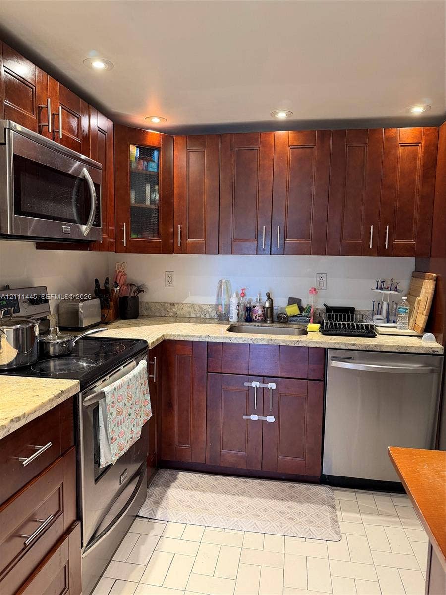 8255 Abbott Avenue, #402, Miami Beach, Miami Beach, FL 33141 Kitchen featuring dark wood-finish cabinetry, stone-style countertops, stainless steel appliances, recessed ceiling lighting, and tile flooring