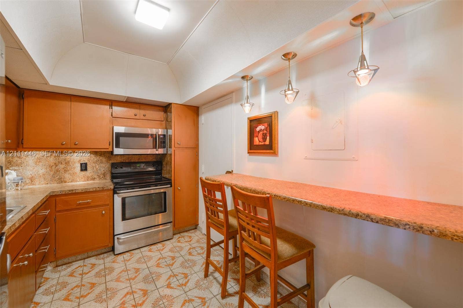 1965 S Ocean Drive, #15M, Hallandale Beach, Hallandale Beach, FL 33009 Kitchen featuring wood cabinetry, stainless steel appliances, speckled stone-finish countertops, tile flooring, and three pendant lights over a built-in breakfast bar