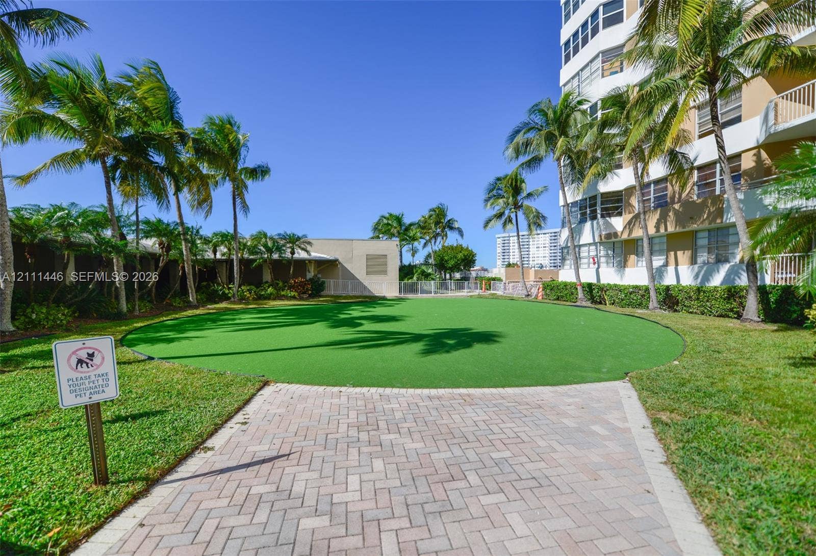 1965 S Ocean Drive, #15M, Hallandale Beach, Hallandale Beach, FL 33009 Manicured artificial turf lawn with paver walkway, mature palm trees, and perimeter landscaping