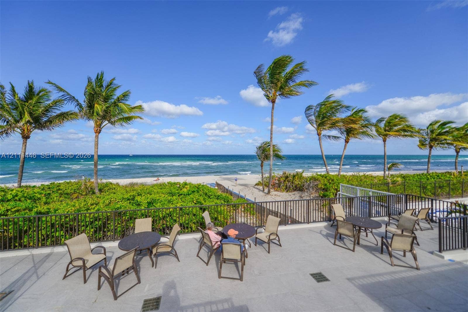 1965 S Ocean Drive, #15M, Hallandale Beach, Hallandale Beach, FL 33009 Elevated stone-paved terrace featuring dark metal railings, tropical palm trees, and an open expanse of oceanfront