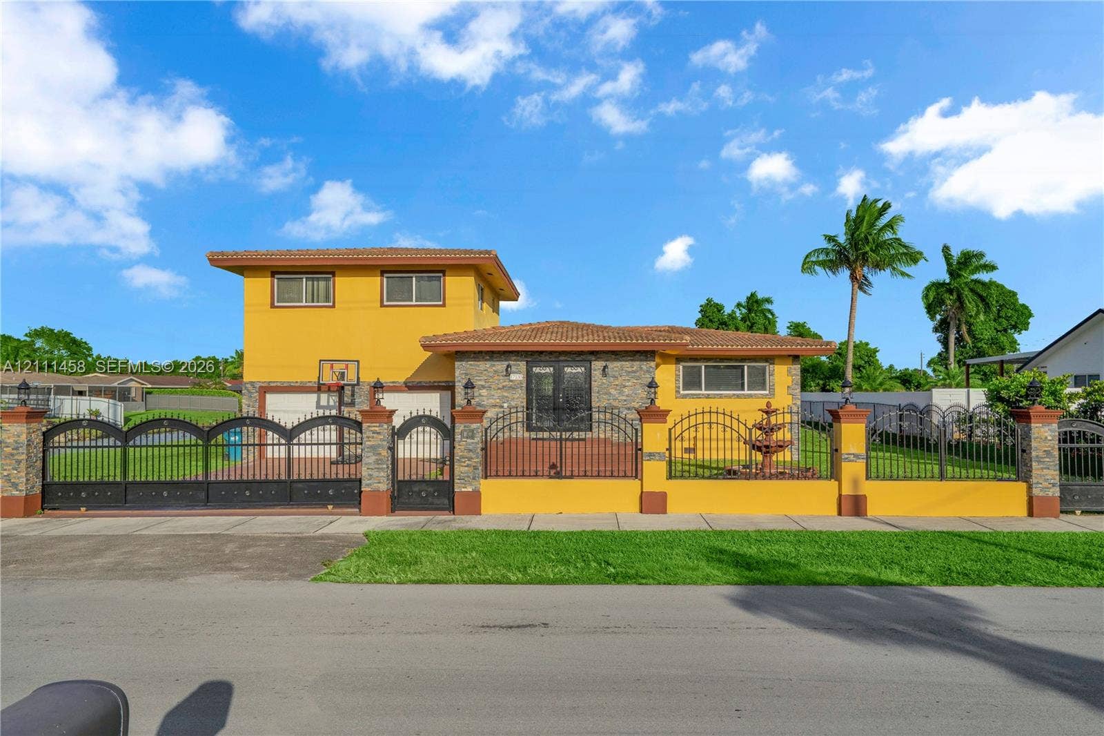 17135 NW 19th Avenue, Miami Gardens, FL 33056 Exterior featuring a two-story stucco facade, decorative stone accents, a multi-tiered fountain, and perimeter wall with wrought iron fencing
