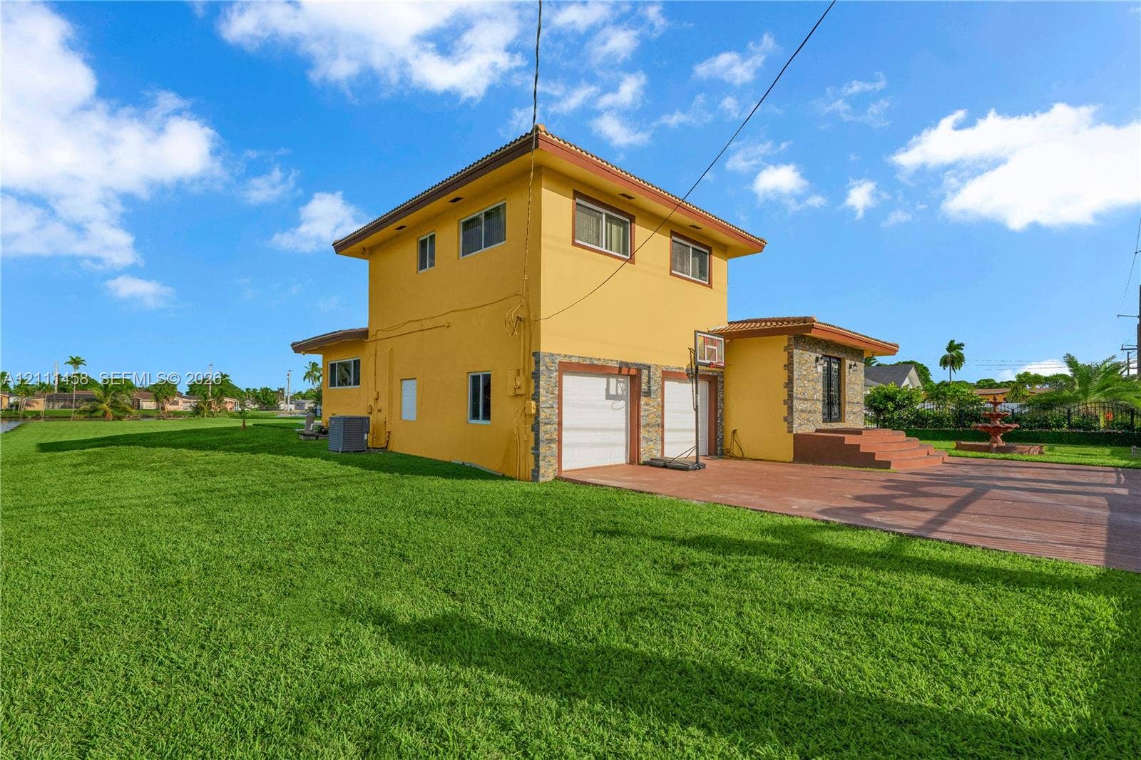 17135 NW 19th Avenue, Miami Gardens, FL 33056 Two-story exterior, stone veneer accents, multi-car garage with white paneled doors, expansive lawn, and paved terrace
