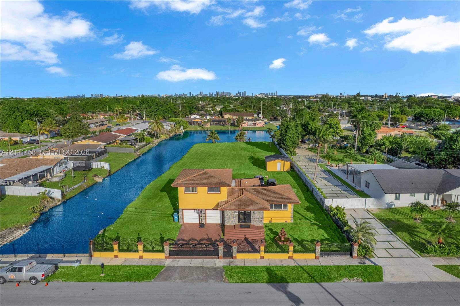 17135 NW 19th Avenue, Miami Gardens, FL 33056 Waterfront residential property featuring expansive lawn space, decorative perimeter fencing, concrete driveway, and attached garage