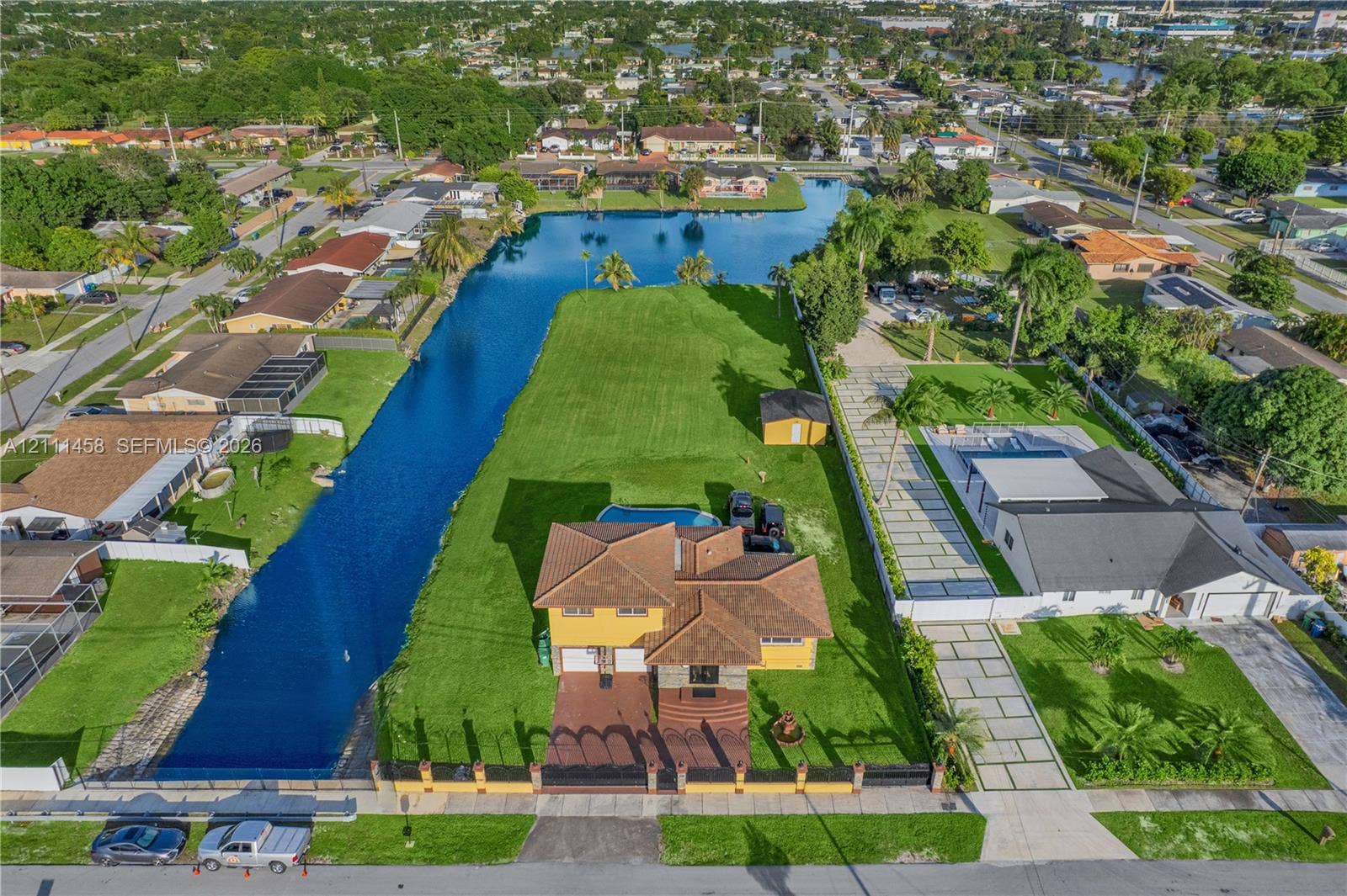 17135 NW 19th Avenue, Miami Gardens, FL 33056 Aerial view featuring a waterfront lot, an in-ground swimming pool, a multi-story residence with a tiled roof, and a paved driveway