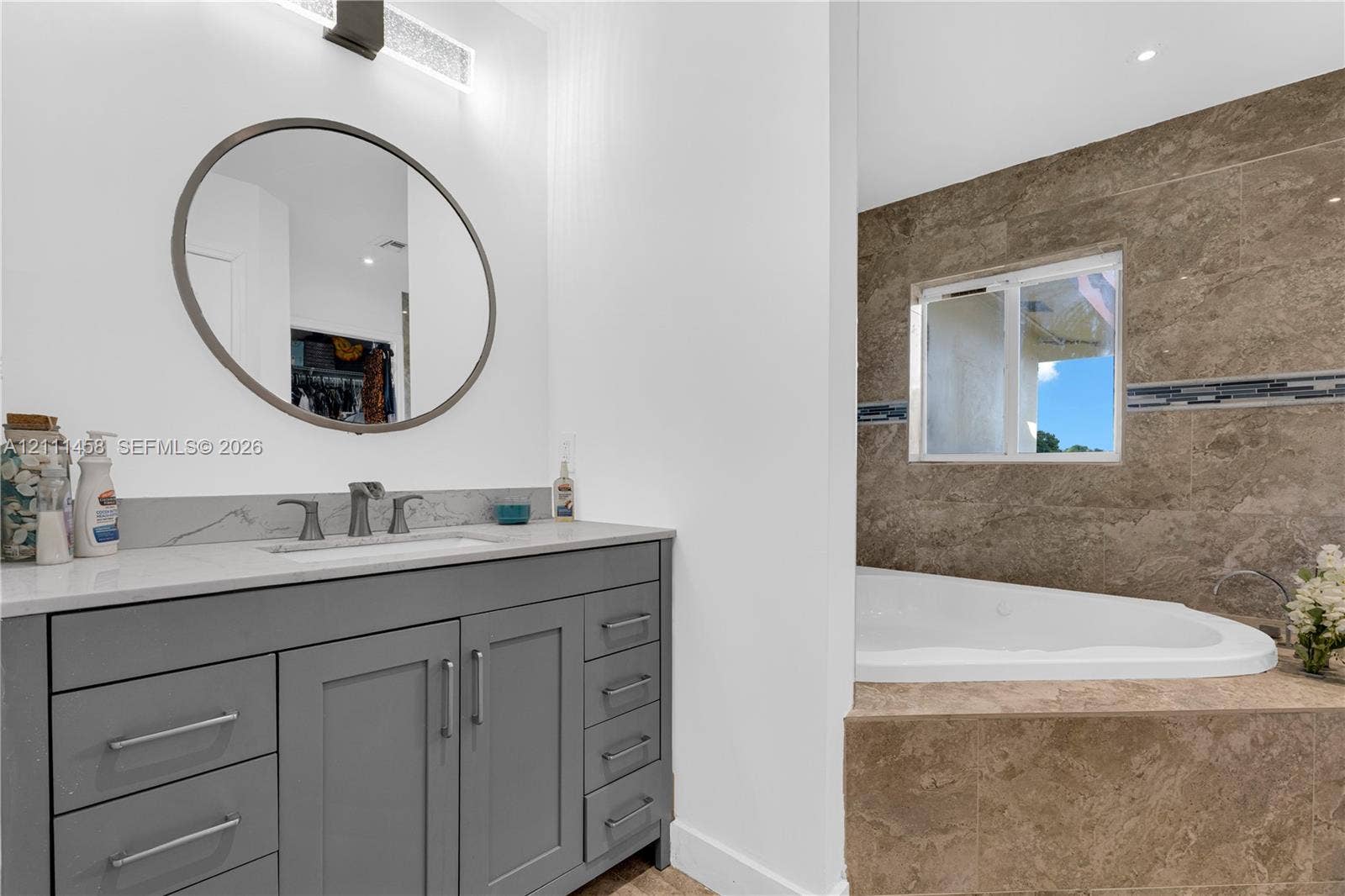 17135 NW 19th Avenue, Miami Gardens, FL 33056 Gray cabinetry vanity an integrated rectangular sink, a circular mirror with metallic framing, and a tiled soaking tub