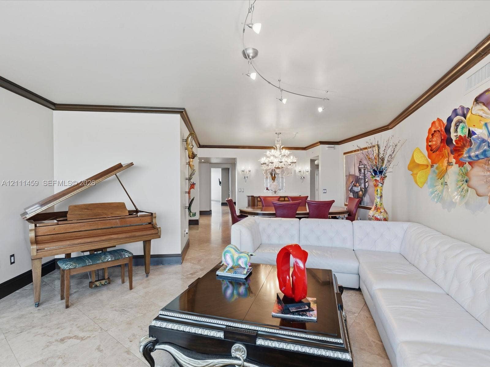 Polished stone flooring, crown molding, multi-point track lighting, and a crystal chandelier
