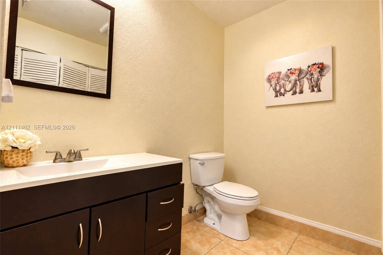 Bathroom featuring a dark-finish vanity with a rectangular basin, two-handle faucet, rectangular mirror with a dark frame, and tiled flooring