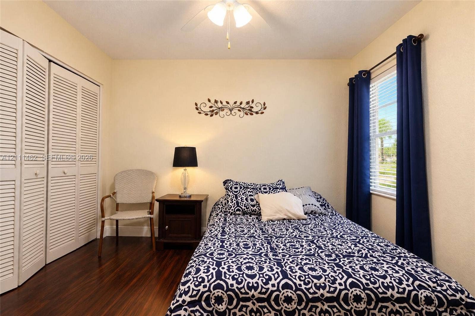 Room featuring wood-finish flooring, dual-panel louvered closet doors, and a ceiling-mounted light fixture with a fan