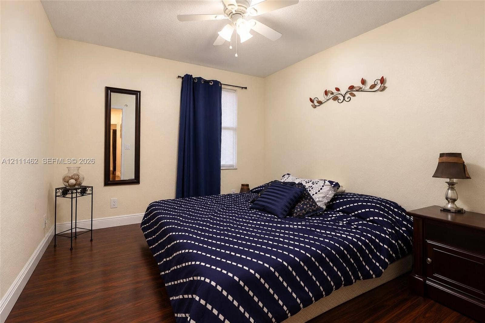 Room featuring wood-finish flooring, a neutral wall palette, a single window with rod-mounted drapery, and an integrated ceiling fan with a multi-light fixture