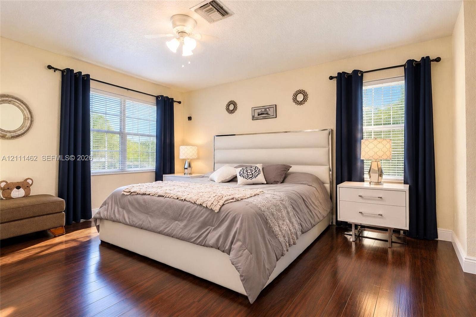 Spacious room featuring wood-finish flooring, dual windows with decorative rods, and a ceiling-mounted light fixture with integrated fan