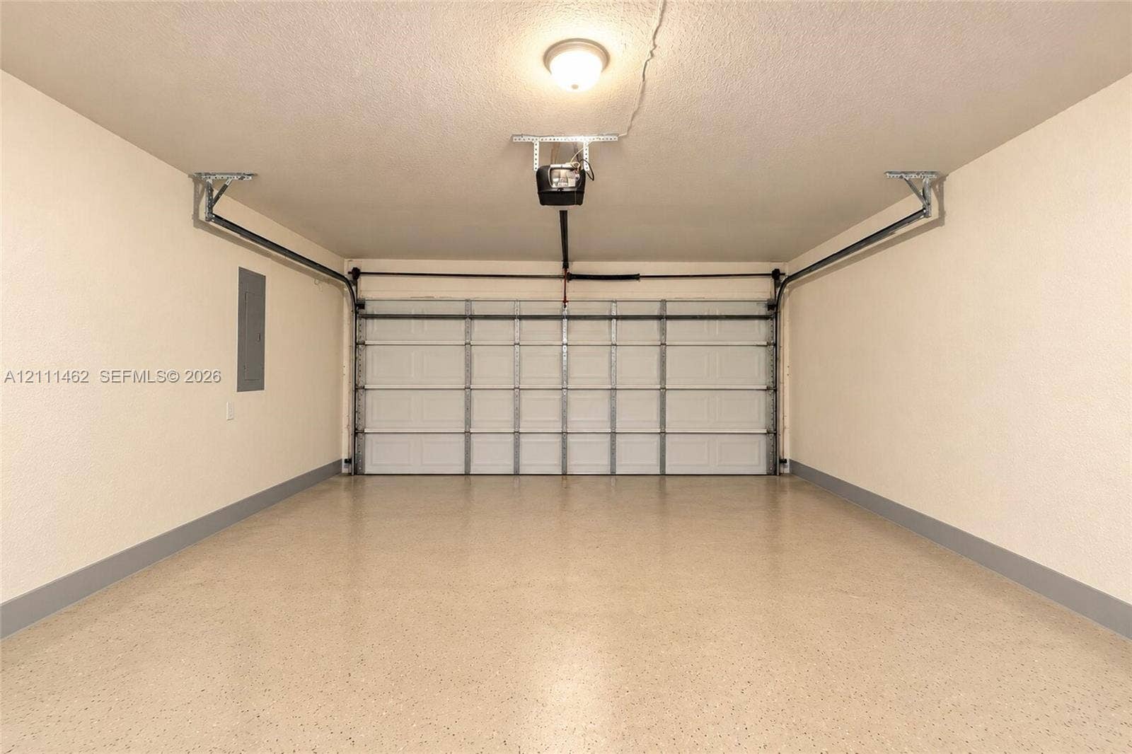 Finished garage featuring a white sectional garage door, epoxy-coated flooring, neutral wall paint, and a ceiling-mounted automatic door opener