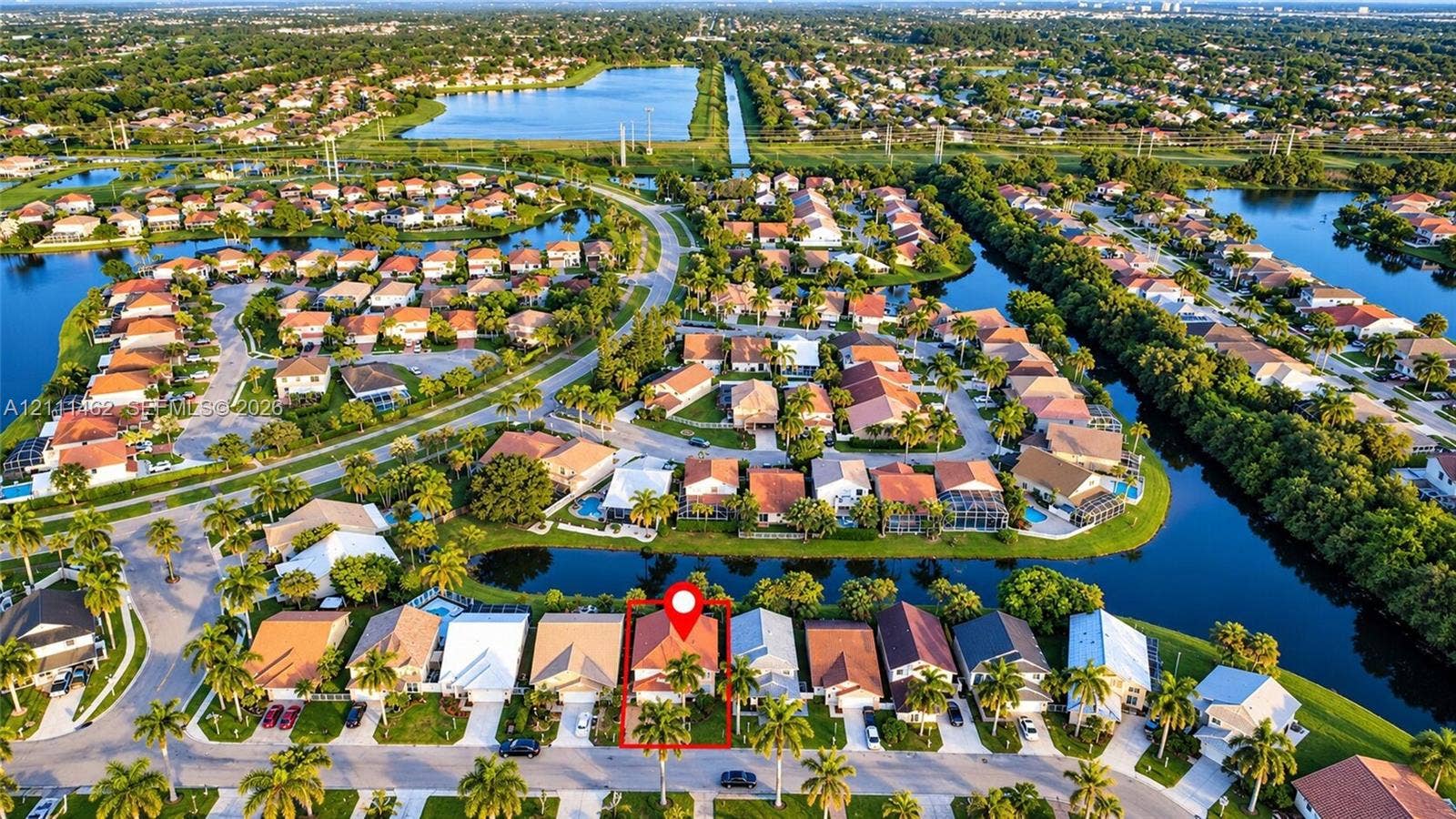 Aerial perspective featuring a multi-pitched tile roof, palm tree landscaping, and a water-front location within a residential community