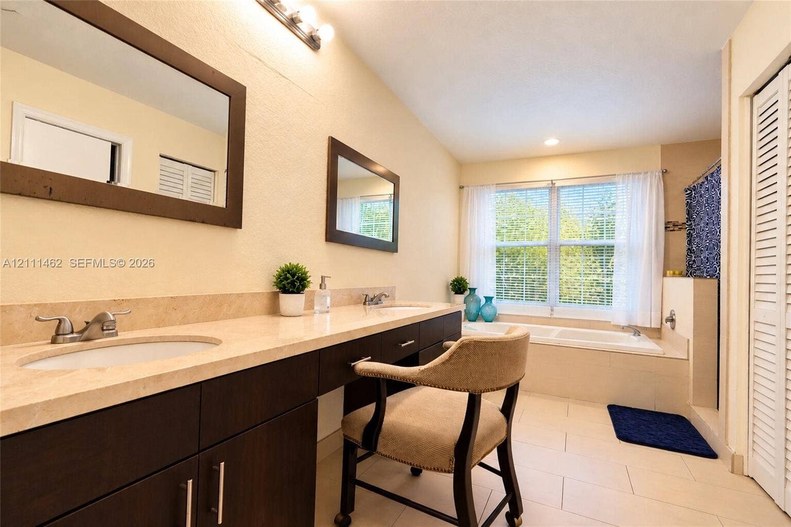 Dual-sink vanity with stone countertop and dark wood-finish cabinetry, framed vanity mirrors, deep soaking tub, and tile flooring