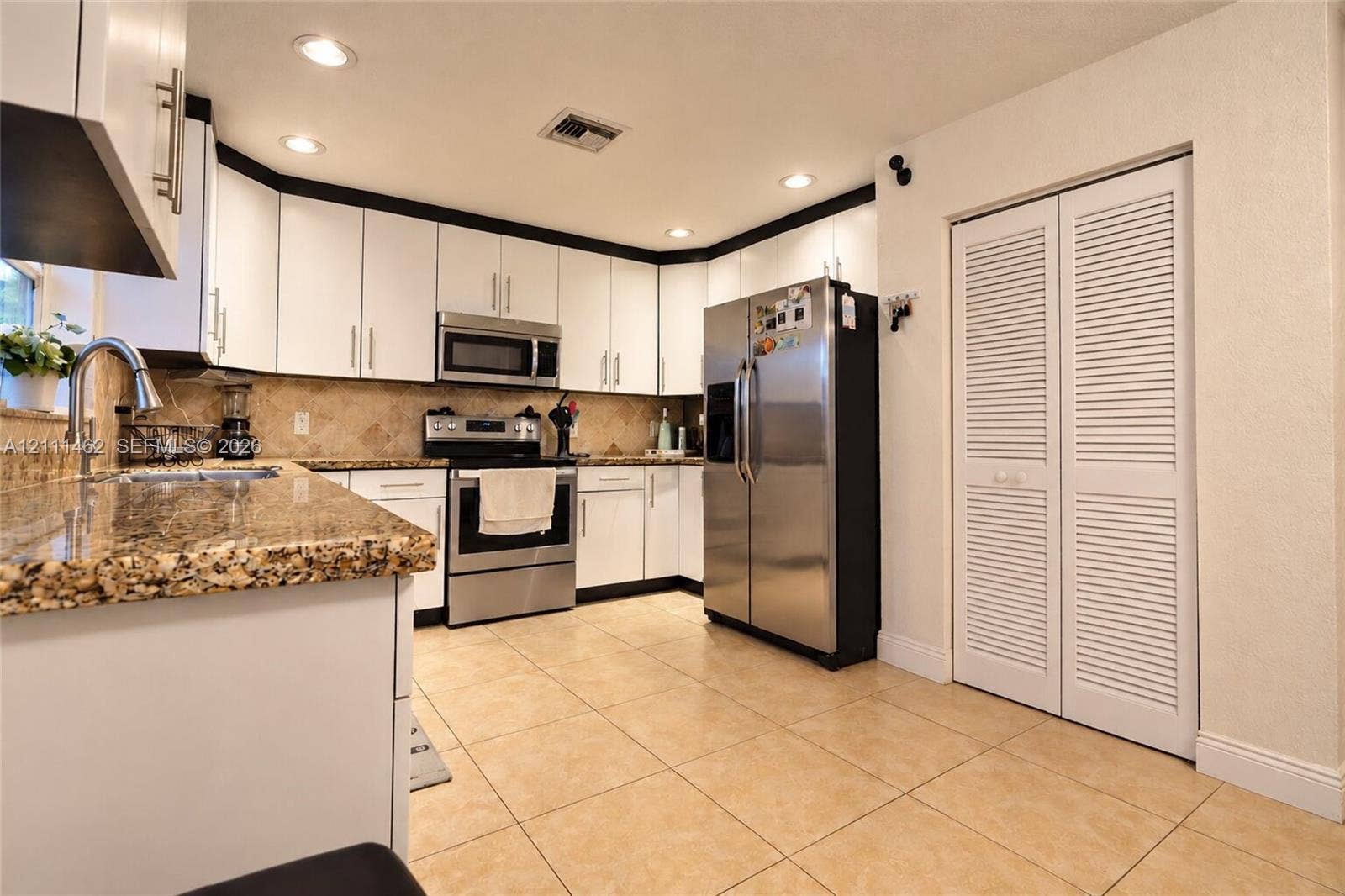 Kitchen featuring white cabinetry, stone-surface countertops, stainless steel appliances, ceramic tile flooring, and louvered closet doors