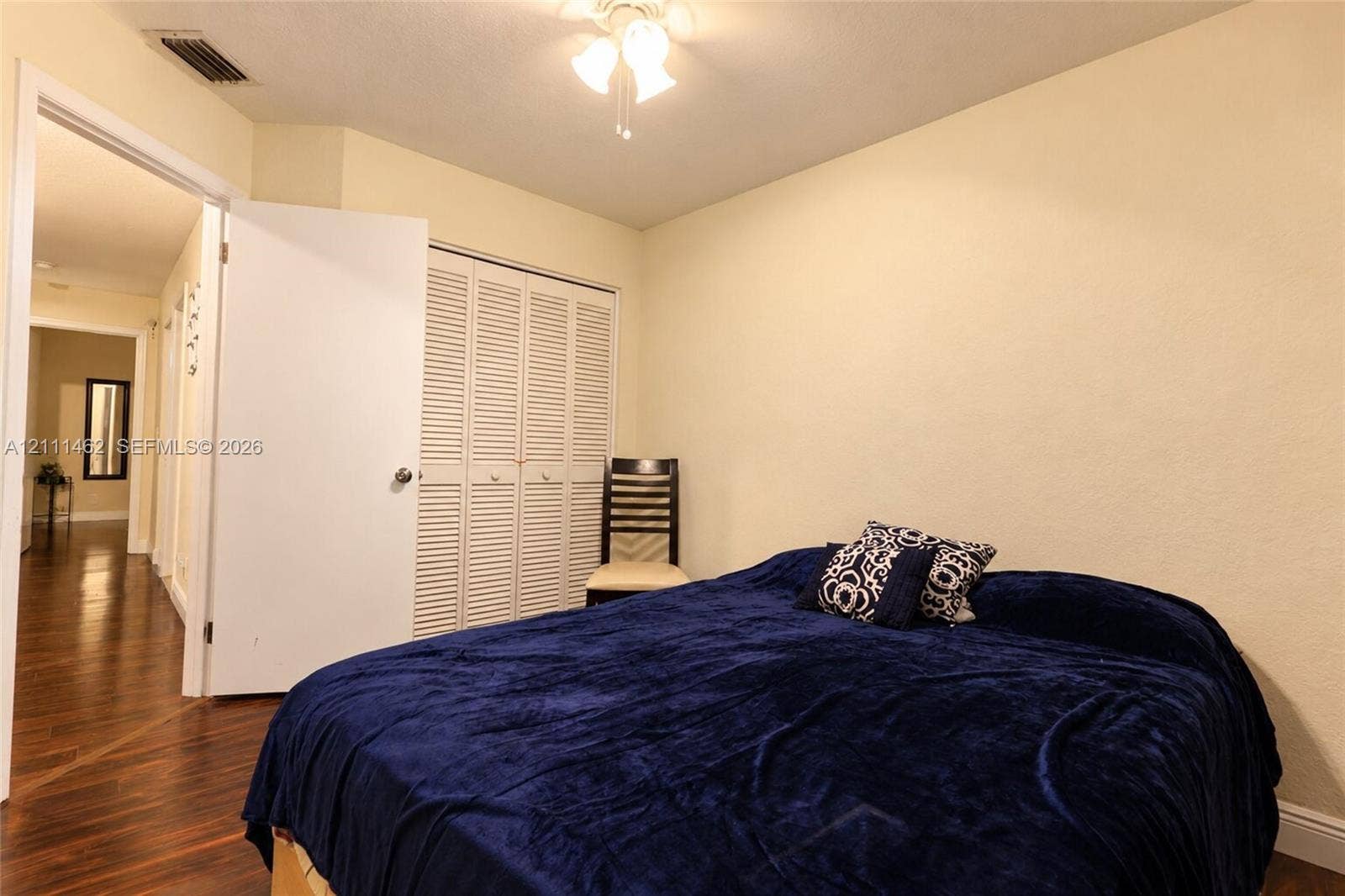 Room featuring wood-finish flooring, ceiling-mounted light fixture, and built-in closet with louvered doors