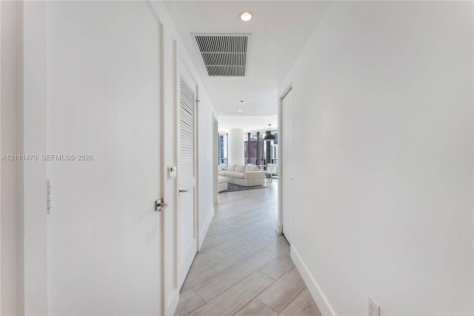 Hallway featuring neutral-tone wood-finish flooring, recessed lighting, and louvered closet doors with brushed-metal hardware