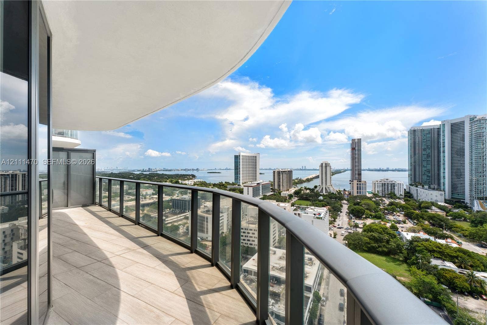 Curved private balcony featuring oversized porcelain tile flooring and glass panel railing