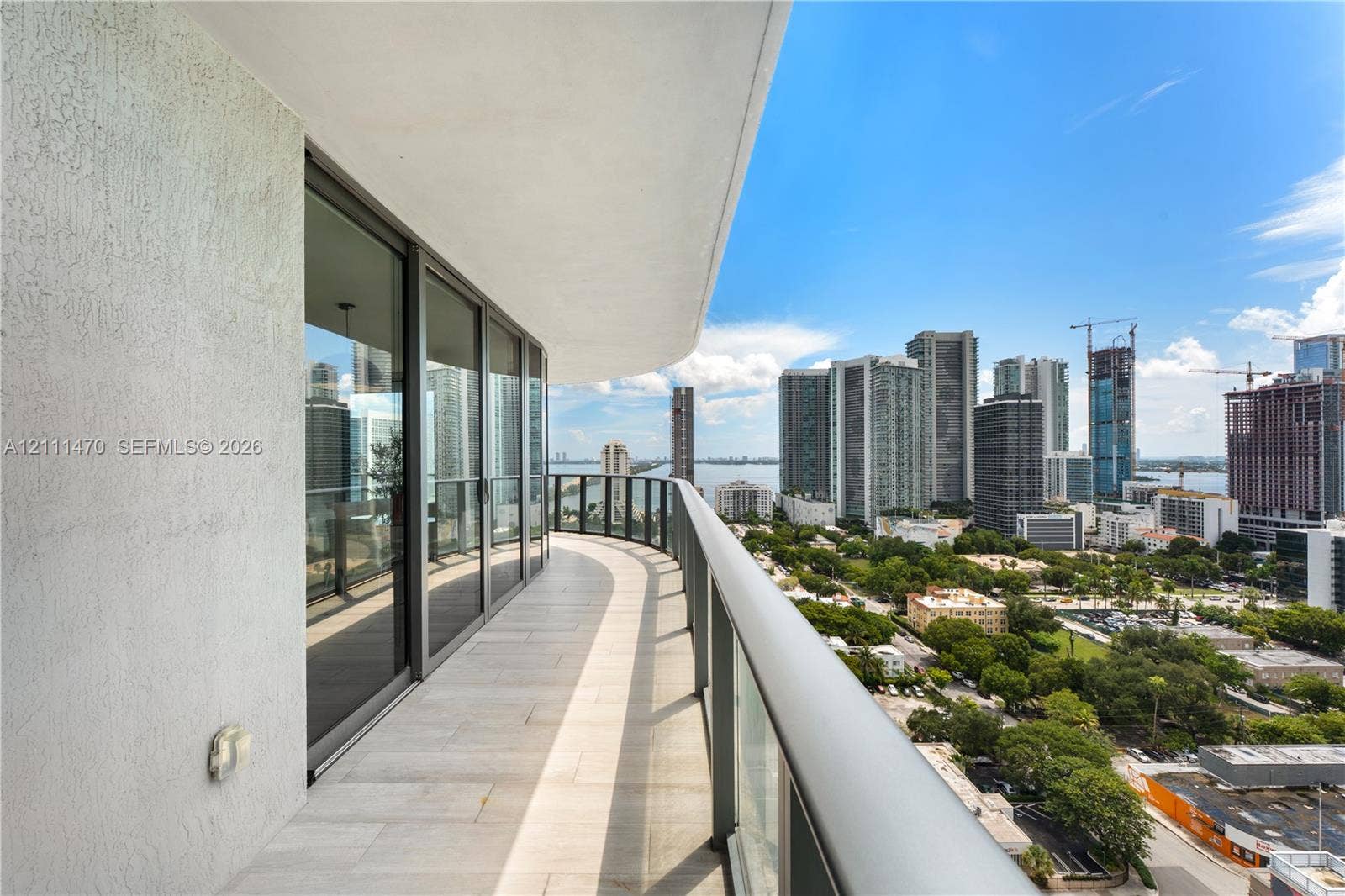 Curved balcony featuring light-toned tile flooring, glass railings, and expansive floor-to-ceiling sliding glass doors