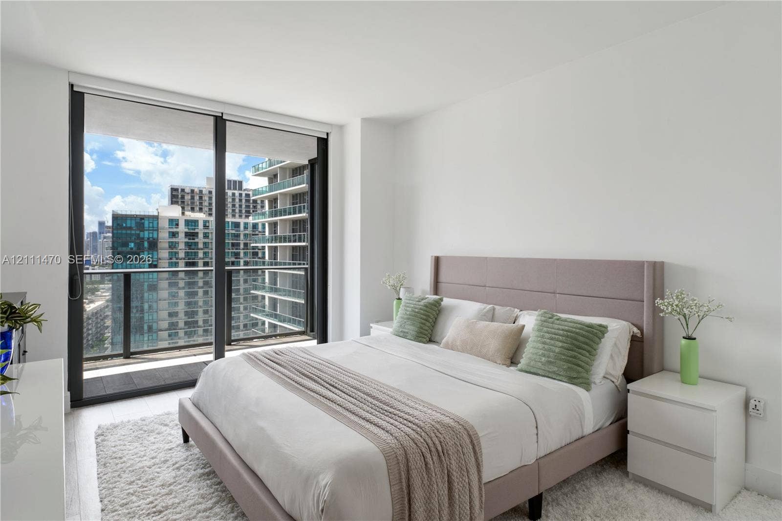 Floor-to-ceiling glass sliding doors, private balcony with metal railing, and neutral wall finishes