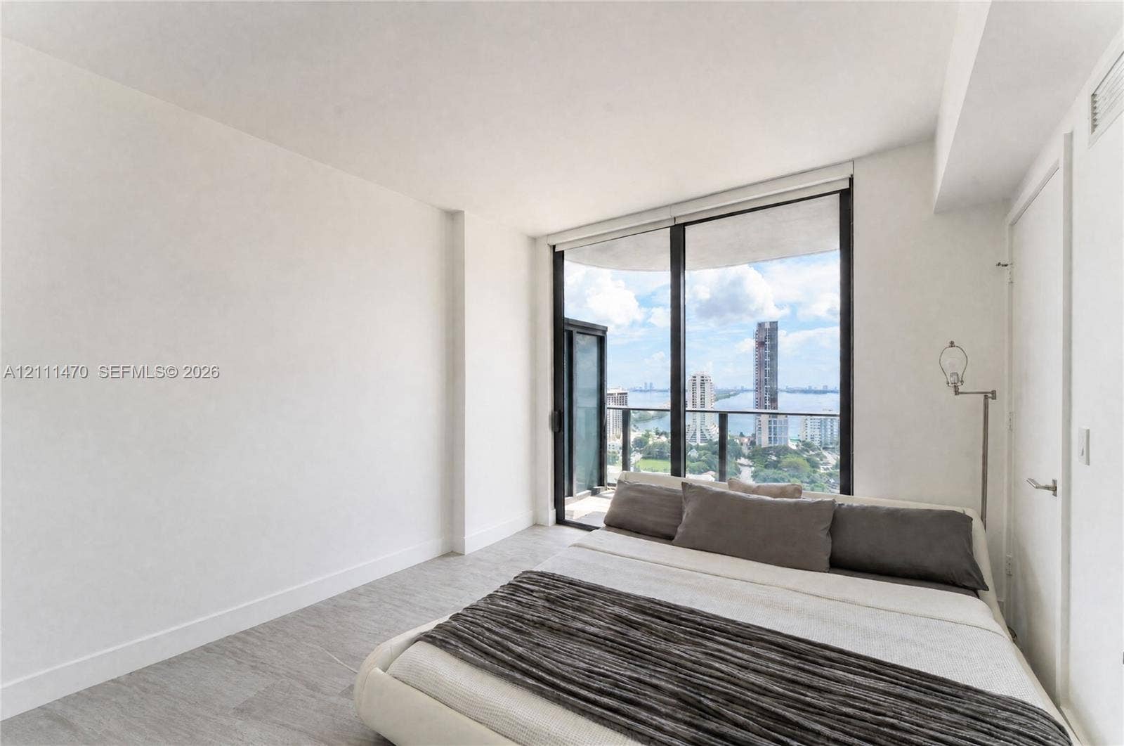 Floor-to-ceiling windows, private balcony access, neutral wall finishes, and wood-finish flooring