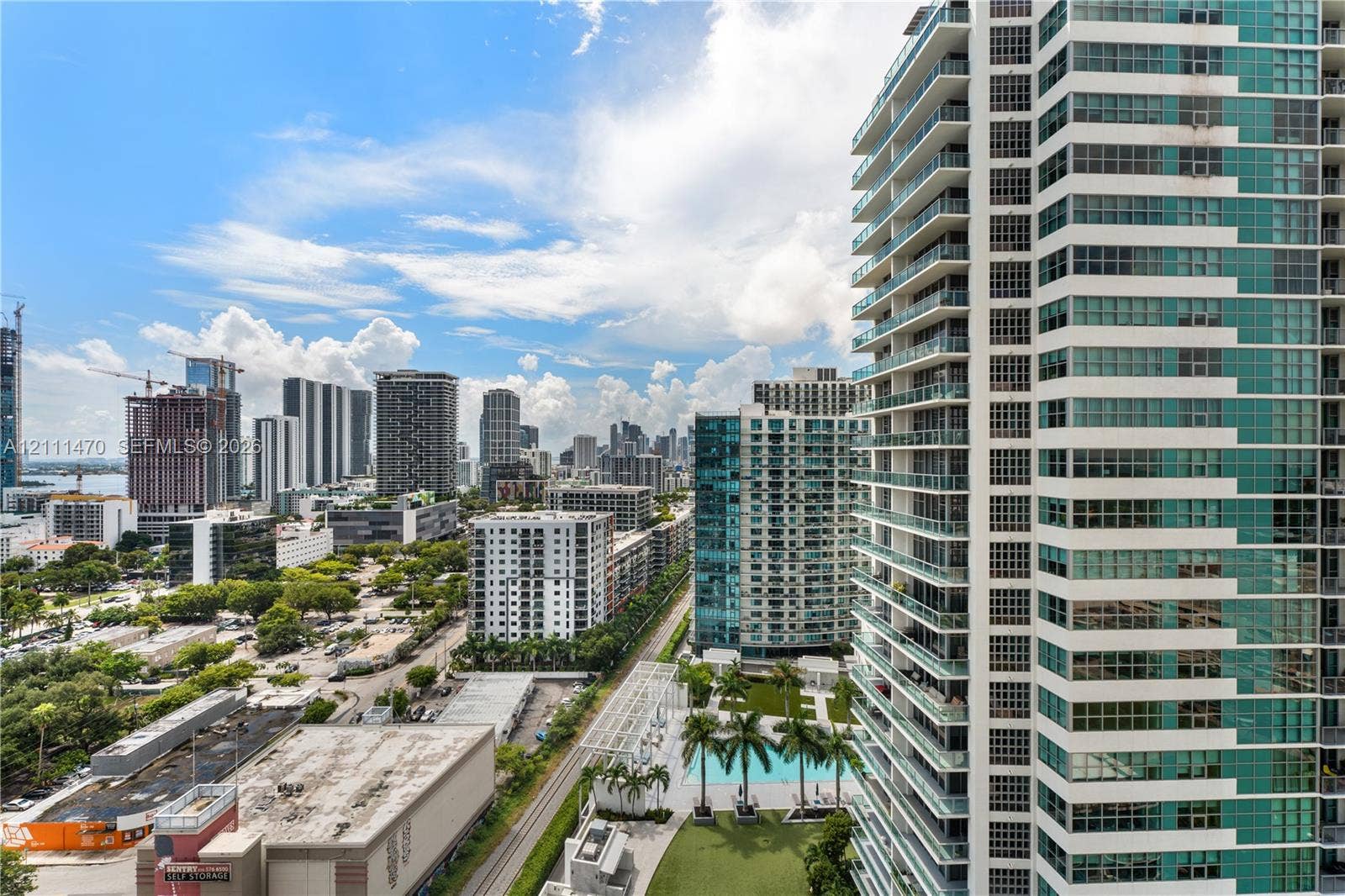 High-rise building exterior featuring glass paneling, floor-to-ceiling windows, and private balconies, complemented by a ground-level swimming pool and manicured green space