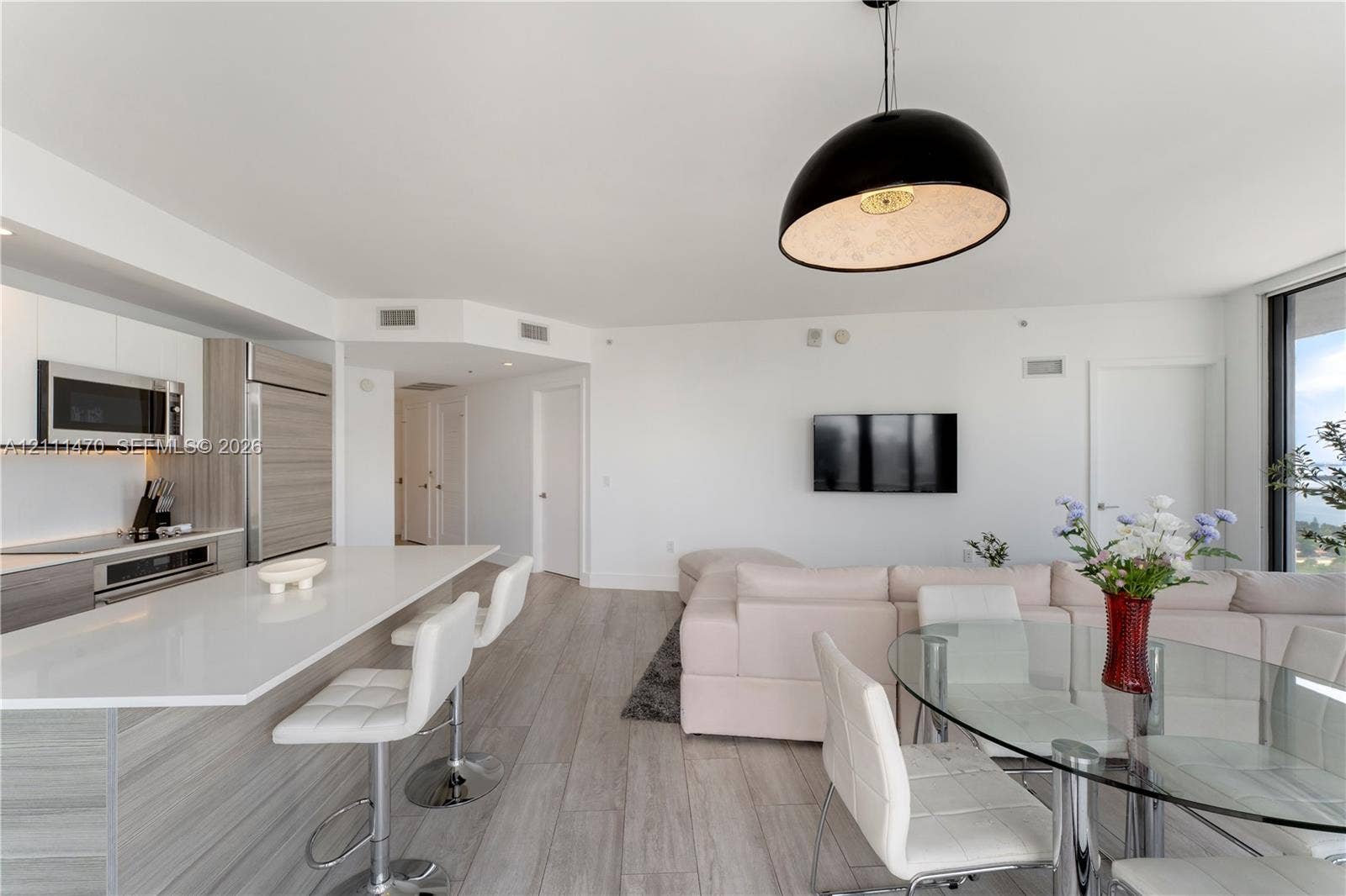 Open-concept kitchen featuring an expansive island with a quartz countertop, integrated cabinetry, stainless steel appliances, and wood-finish flooring with a dome pendant light fixture