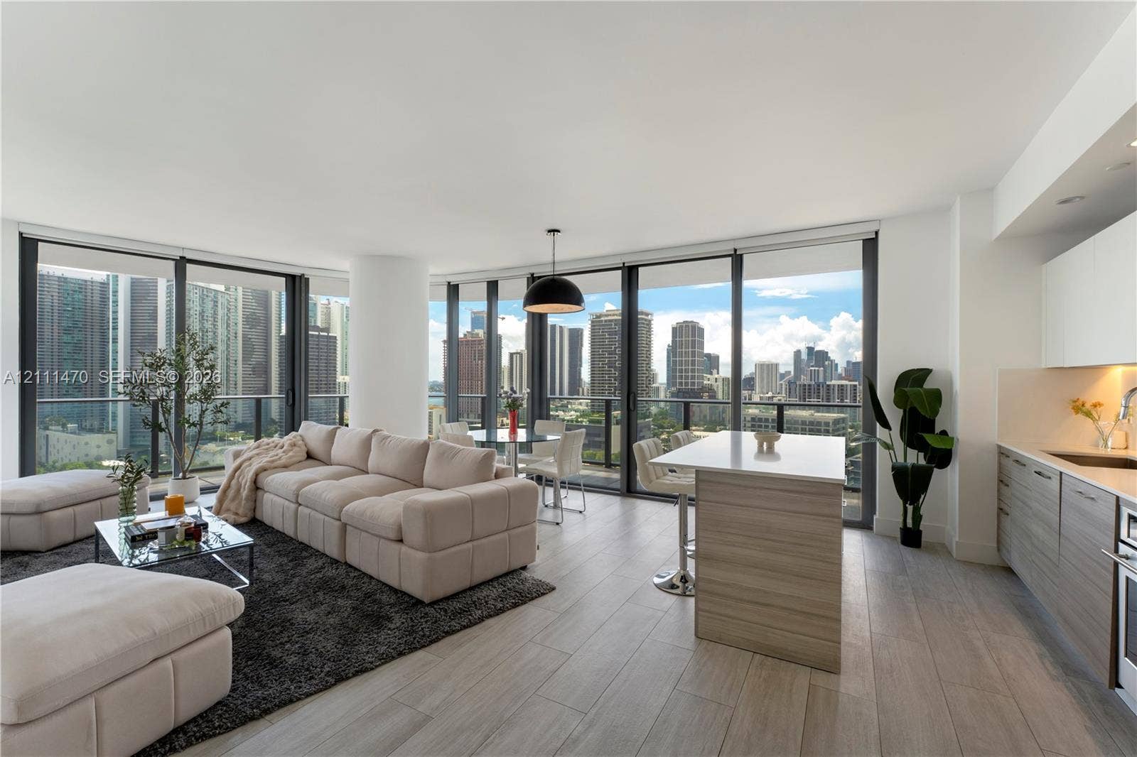 Open-concept living space featuring floor-to-ceiling windows, wood-finish flooring, a kitchen island with stone countertop, and contemporary pendant lighting