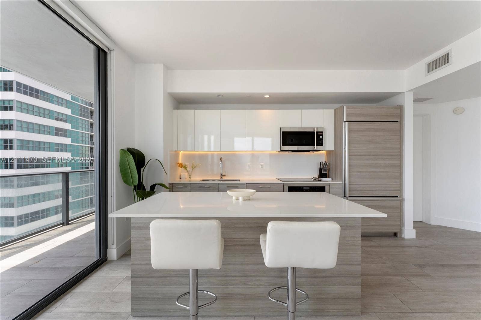 Kitchen featuring a white quartz island, high-gloss flat-panel cabinetry, integrated refrigerator, wood-finish lower cabinetry, and floor-to-ceiling glass sliding doors