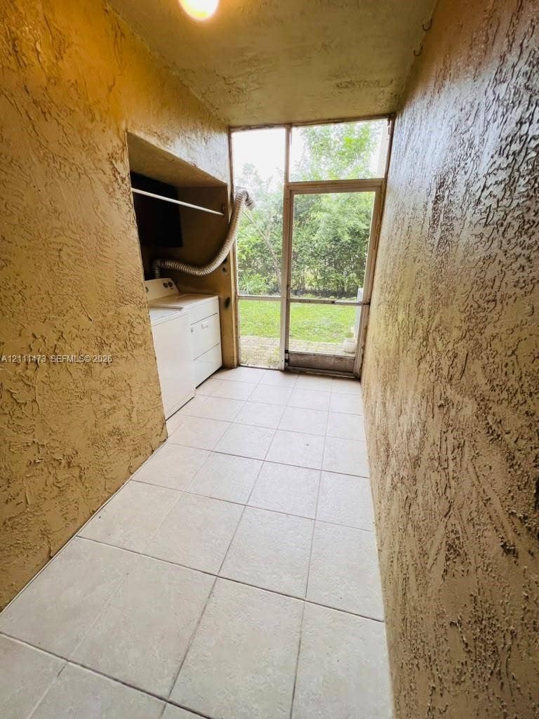11101 Royal Palm Boulevard, #113, Coral Springs, Coral Springs, FL 33065 Enclosed utility area featuring textured walls, tile flooring, built-in recessed cabinetry, and a screened door leading to an outdoor space