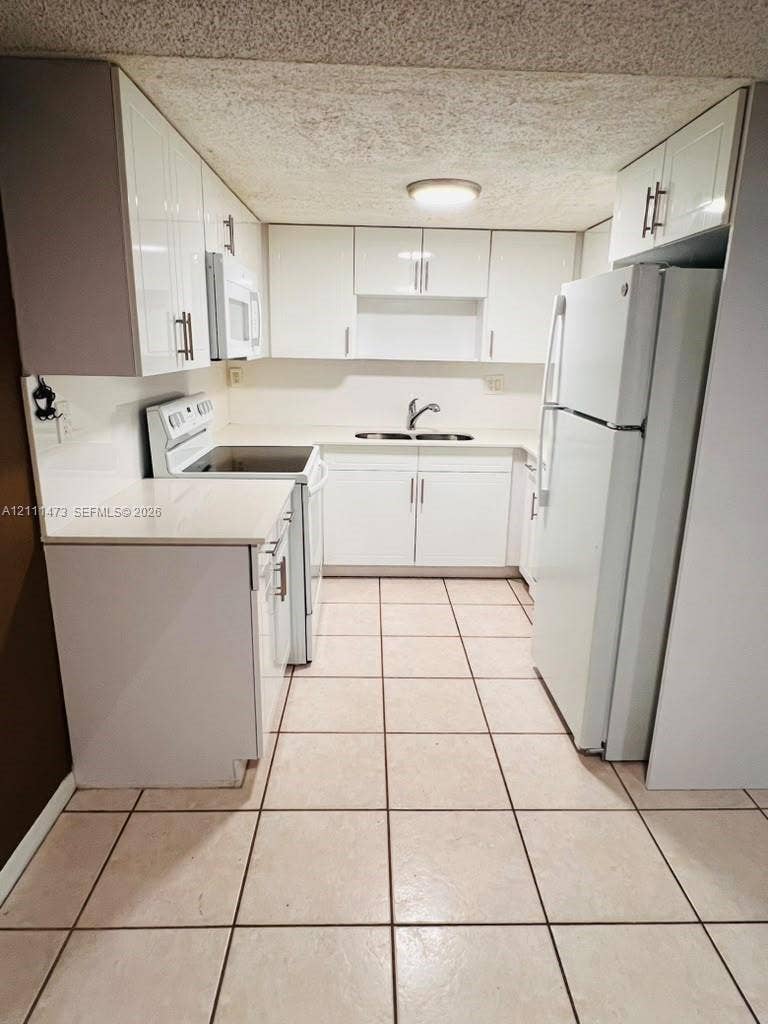 11101 Royal Palm Boulevard, #113, Coral Springs, Coral Springs, FL 33065 Kitchen featuring high-gloss white cabinetry, solid-surface countertops, dual-basin stainless steel sink with arch-neck faucet, and ceramic tile flooring