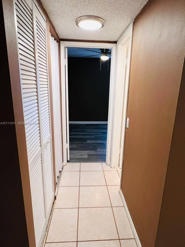 11101 Royal Palm Boulevard, #113, Coral Springs, Coral Springs, FL 33065 Hallway featuring ceramic tile flooring, floor-to-ceiling white louvered closet doors, and flush-mount ceiling lighting