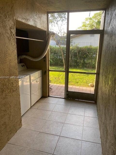 11101 Royal Palm Boulevard, #113, Coral Springs, Coral Springs, FL 33065 Laundry area featuring a built-in recessed shelf, light-colored tile flooring, stucco walls, and a screen door with exterior access to a paved patio area